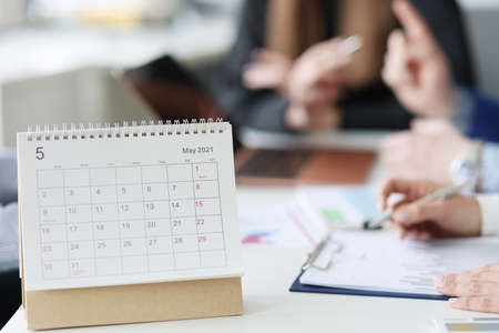 Calendar for May is on desktop against background of employeesの写真素材