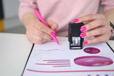 Woman holds pen and puts stamp on documents with business chartsの写真素材