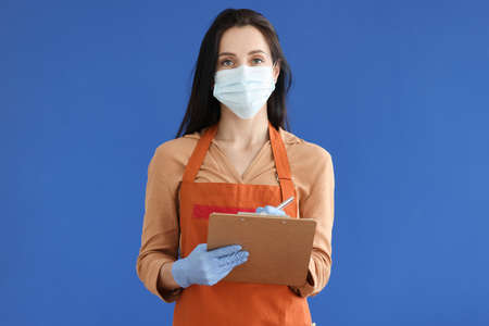 Woman waiter in protective mask and gloves writing down order on blue backgroundの写真素材