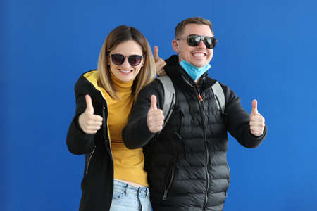Young man and woman in sunglasses and warm clothes showing thumb upの写真素材