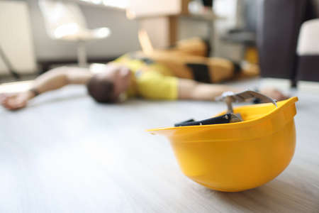 Yellow safety helmet is lying on floor near dead worker conceptの写真素材