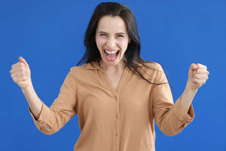 Contented woman with folded fists shouting on blue backgroundの写真素材