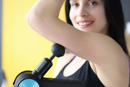 Young woman doing shoulder muscle massage with percussion massager closeup