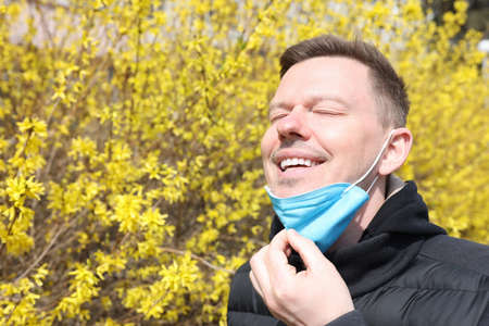 Young man taking off protective respirator from face near flowering treeの写真素材