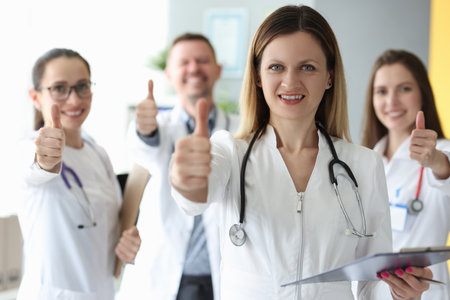 Woman doctor showing thumb up against background of colleaguesの写真素材