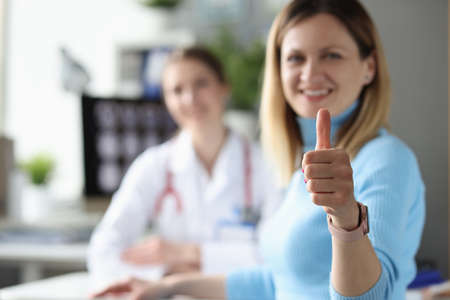 Woman patient demonstrates thumbs up gesture at doctor appointmentの写真素材