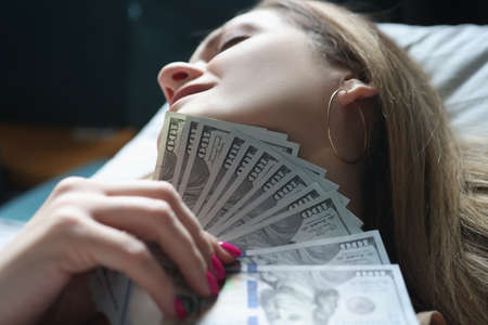 Young woman lying in bed with money in her handsの写真素材