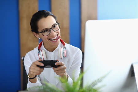 Joyful woman holds game joystick in her hands and plays online games in office