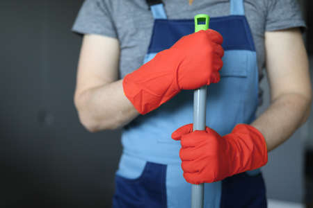 Hands of cleaner in yellow gloves holding mop handleの写真素材