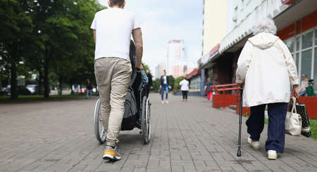 Man rolls a seated woman in wheelchair down street in cityの写真素材