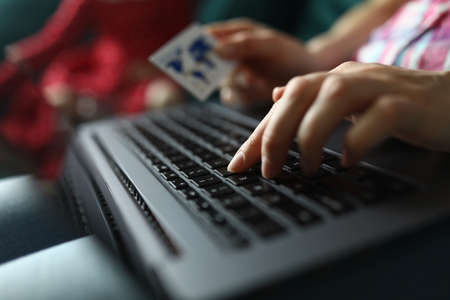 Woman hand holds plastic credit bank card and works on keyboardの写真素材