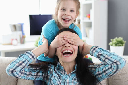 Little girl closing eyes to mom sitting on couchの写真素材