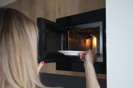 Woman putting plate of food in microwave at home closeup