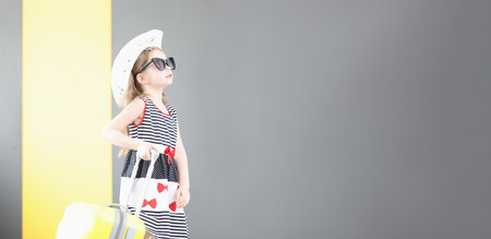 Little girl in sunglasses and hat walking with suitcase in her handの写真素材
