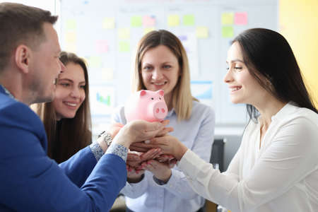 Group of people holding pink piggy bank in officeの写真素材