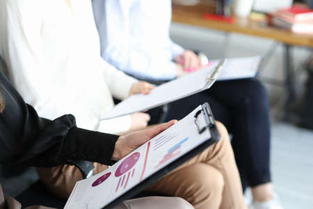 Hands of business employees with documents and charts with financial indicators sitting on chairs