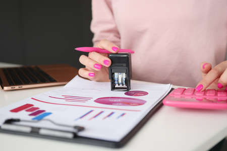 Women hands put stamp on documents and count on calculatorの写真素材