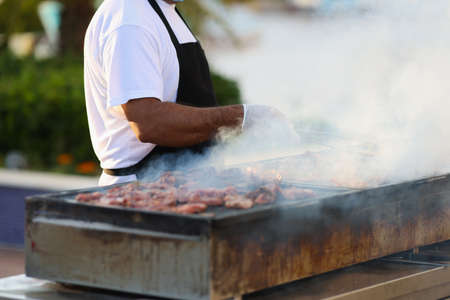 Cook prepares meat on grill on street