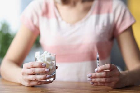 Woman sitting at table and holding glass of sugar and insulin syringe closeupの写真素材