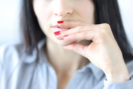 Pensive young woman touching lips with hands with red manicure closeupの写真素材