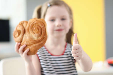 Little girl eating big bun and showing thumb up closeupの写真素材