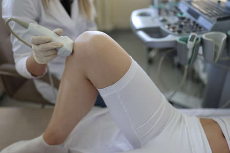 Doctor doing ultrasound examination of knee joint to woman in clinic closeupの写真素材