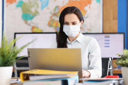 Woman in protective medical mask works at laptop