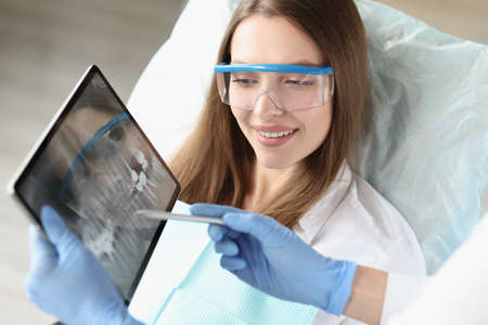 Dentist shows X-ray of a woman jaw on tablet to patient