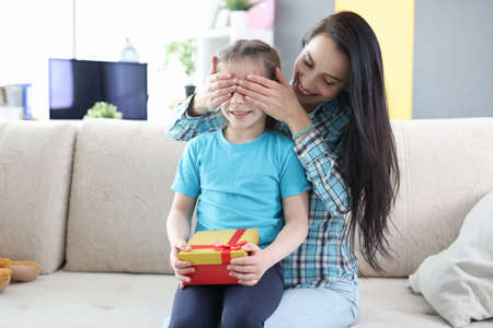 Young mother closes her daughter eyes and gives her gift