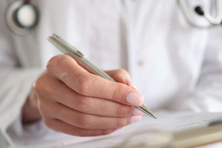Woman doctor writes patient data into documents with pen