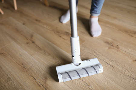 Woman cleaning floor in apartment with vacuum cleaner closeup