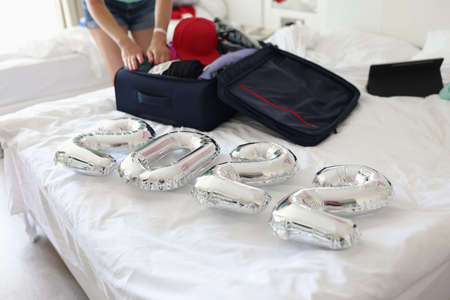Silver balloons with numbers 2022 lying on bed with suitcase in bedroom closeupの写真素材