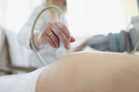 Doctor conducting ultrasound examination of fetus of pregnant woman in clinic closeup