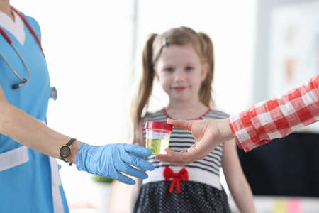 Mother giving doctor jar of urine analysis in front of little girl closeupの写真素材
