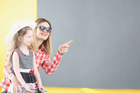 Mother in sunglasses showing her finger to little girl in hat