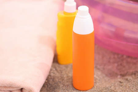 Two bottles of sunscreen stand on sand on beach
