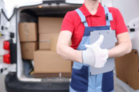 Loader driver in uniform holds a thumbs up in background of car with boxesの写真素材
