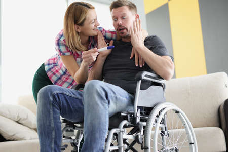 Young woman showing positive pregnancy test to disabled man in wheelchair