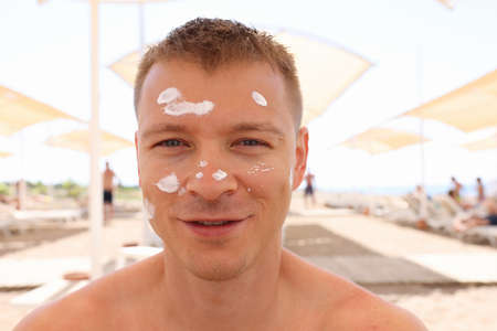Man sitting on beach with sunscreen on his faceの写真素材