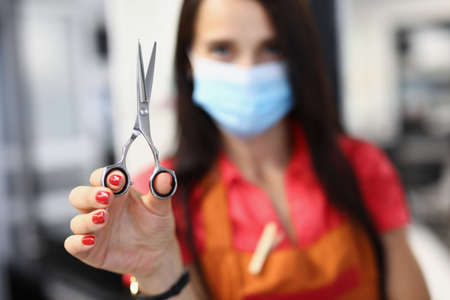 Woman hairdresser in medical protective mask holds scissors in handの写真素材