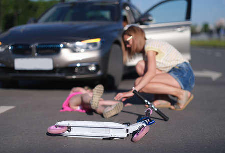 Children scooter lying on background of injured little girl and woman driver of car closeup
