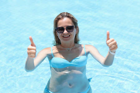 Portrait of smiling young woman in sunglasses showing thumbs up gesture in pool