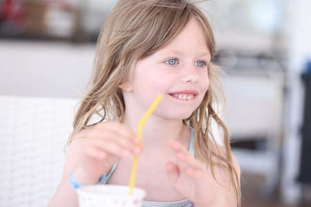 Little girl in swimsuit drinking cocktail from straw on beachの写真素材