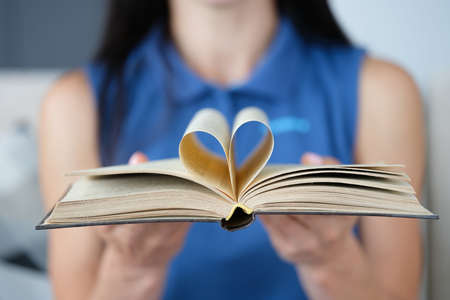 Woman is holding book with a page in shape of heart folded in centerの写真素材