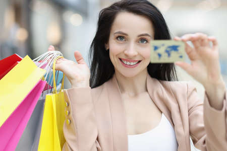 Portrait of young smiling woman holding credit bank card and shopping bags in handの写真素材