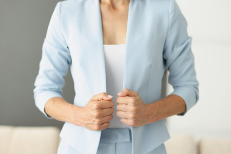 Woman in blue suit holding edges of her jacket with her hands closeupの写真素材