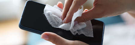 Female hand wipes smartphone with disinfectant napkin from bacteriaの写真素材