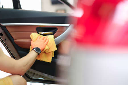 Male hand hold yellow microfiber towel and wipes the door with leather panel closeupの写真素材