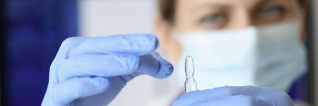 Nurse in mask and gloves holding ampoule of medicine closeup