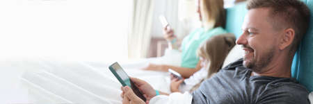 Parents with child lie on bed with smartphones